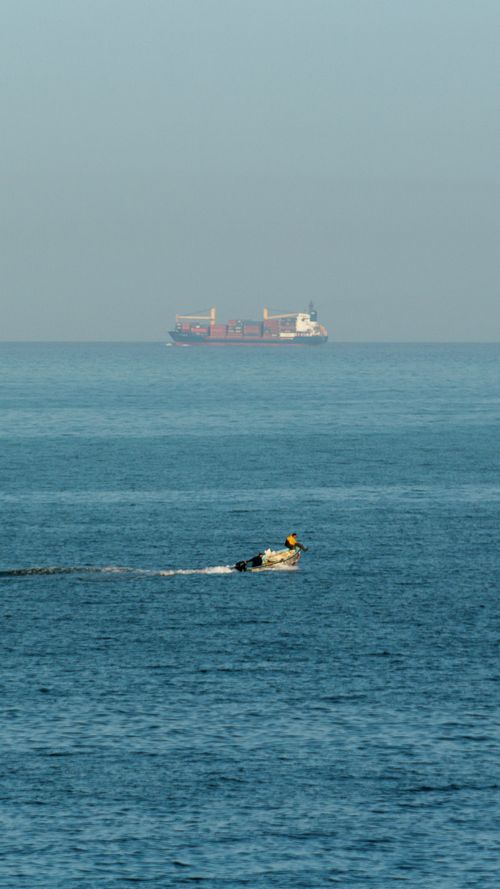 Free Serene ocean scene featuring a distant cargo ship and motorboat under clear skies. Stock Photo