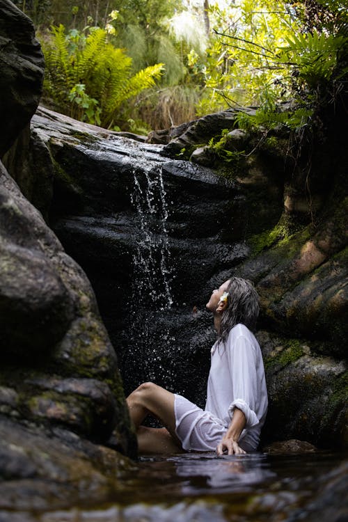 Woman Sitting in Creek with Waterfall