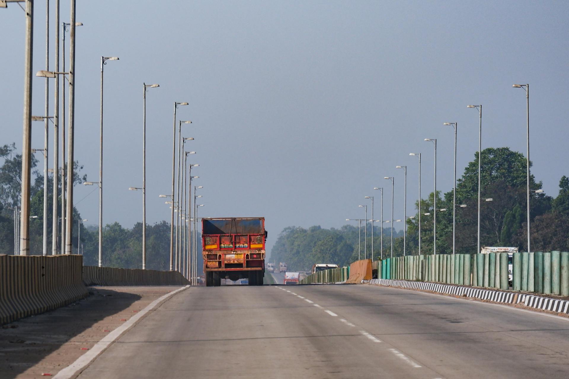 Wide highway view with a truck and rows of street lamps on a clear day.