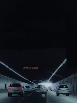 Photo by Beard Kid Dimly lit Dubai tunnel with 'Left Lane Closed' sign and flowing traffic at night.