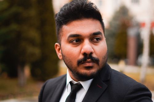Free Elegant portrait of a young man in a black suit with a contemplative expression, captured outdoors. Stock Photo