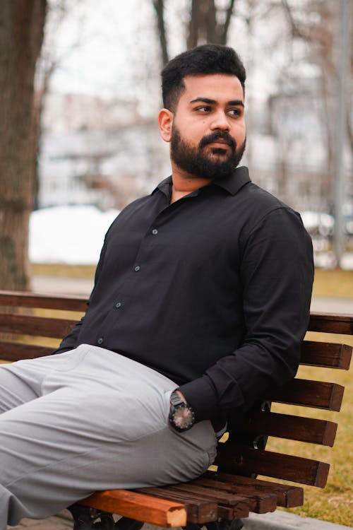 A man in a black shirt and grey pants sitting on a bench