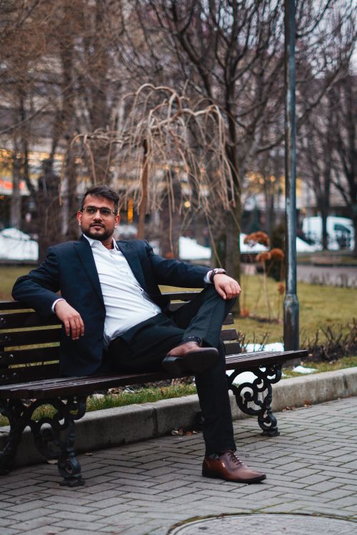 Free Confident man in a blazer relaxing on a park bench, showcasing elegant style. Stock Photo