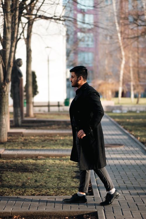 Free Stylish man in a black coat walking along a city park path on a sunny autumn day. Stock Photo