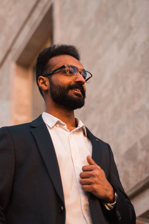 Free Portrait of a confident man with a beard and glasses in business attire, standing outdoors. Stock Photo