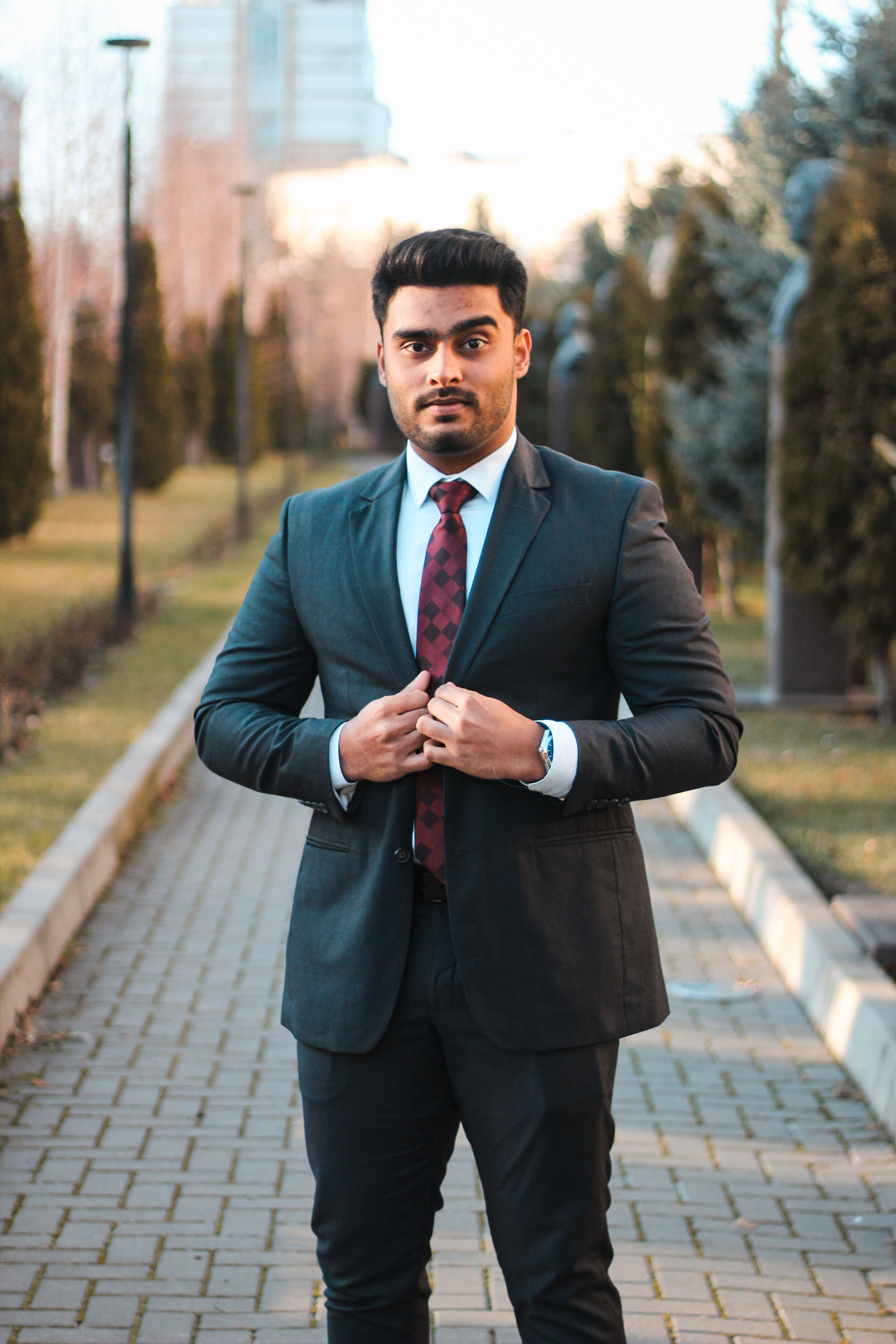 Portrait of a man in a suit standing confidently in an outdoor city park.