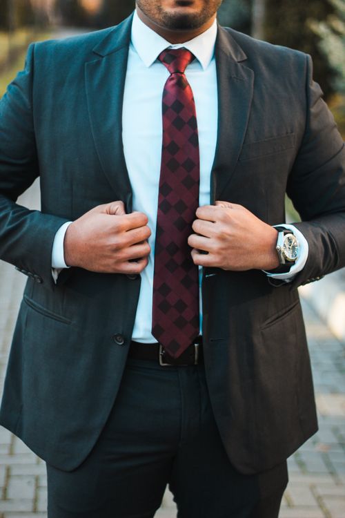 Free Confident man in elegant suit adjusts his tie, showcasing style and sophistication outdoors. Stock Photo