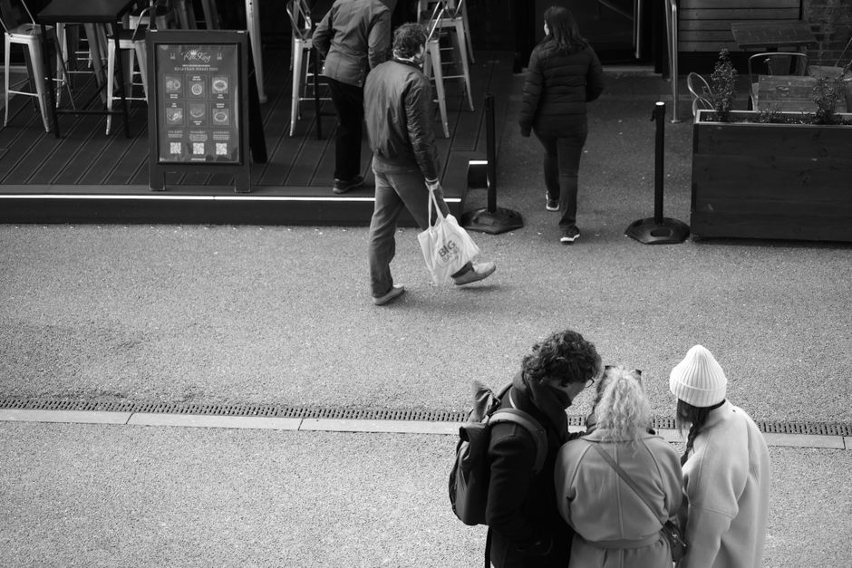 Black and white photo of people interacting near an outdoor café, highlighting city life