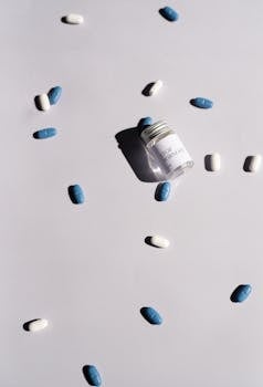 Jar of pills and scattered blue and white tablets on a white surface, highlighting healthcare themes.