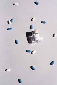 Artistic arrangement of blue and white pills scattered around a bottle on a white background.