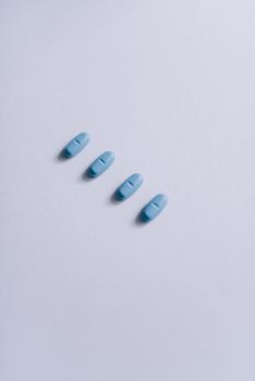 Close-up of four blue pills arranged on a clean white surface.