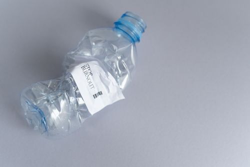 Free Close-up of a crushed plastic bottle with a 'STOP BURNOUT' label, emphasizing environmental awareness. Stock Photo