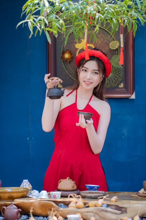 Free A woman in a traditional red dress enjoys tea preparation against a vibrant backdrop. Stock Photo