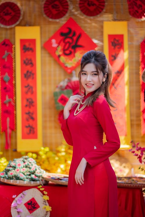 Free Portrait of an elegant Asian woman in a traditional red dress, smiling in a vibrant festival setting. Stock Photo