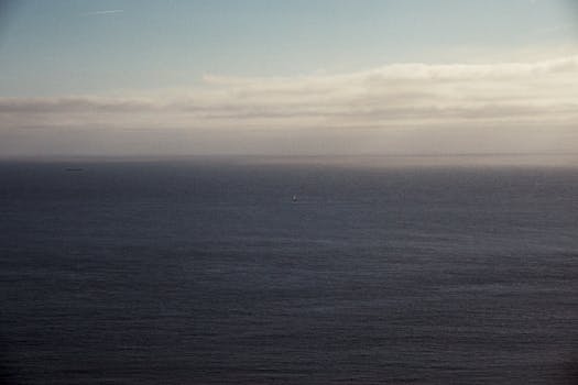 Serene seascape with a vast ocean, distant clouds, and a hint of sunlight.
