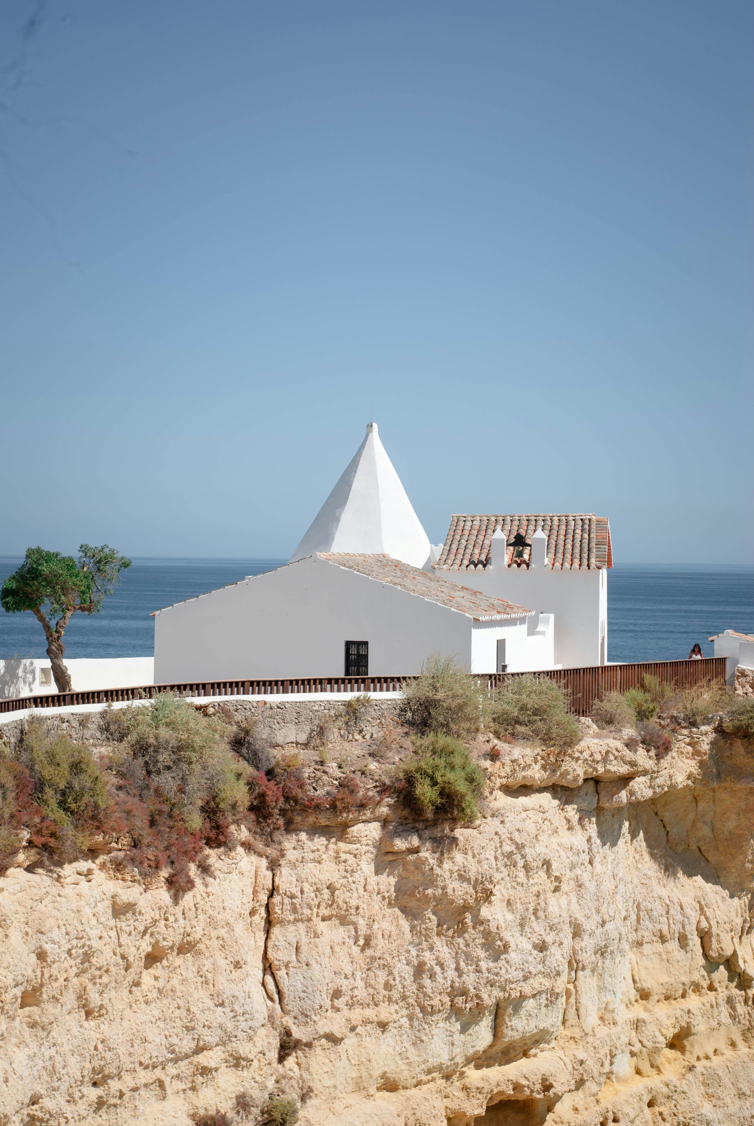 Scenic view of a white building perched on a cliff with an ocean backdrop under a clear sky.
