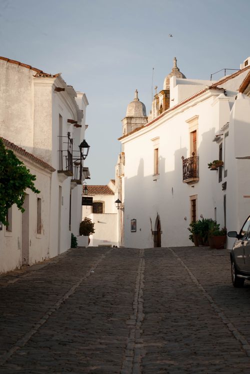 Free Explore a quiet cobblestone street in a historic Portuguese town, featuring classic white architecture. Stock Photo