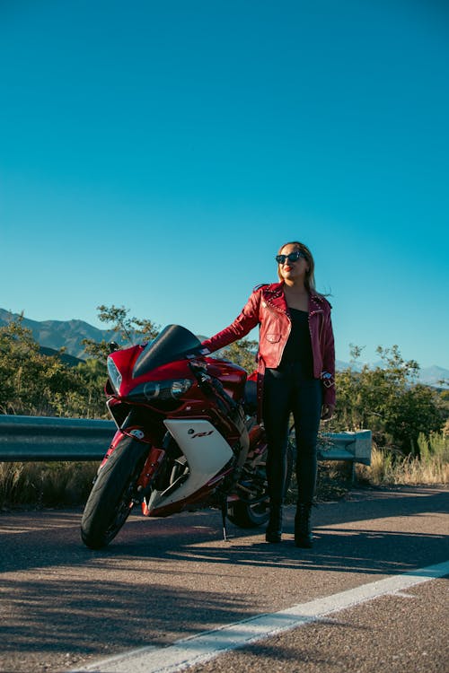 A woman in a red leather jacket is standing next to a motorcycle