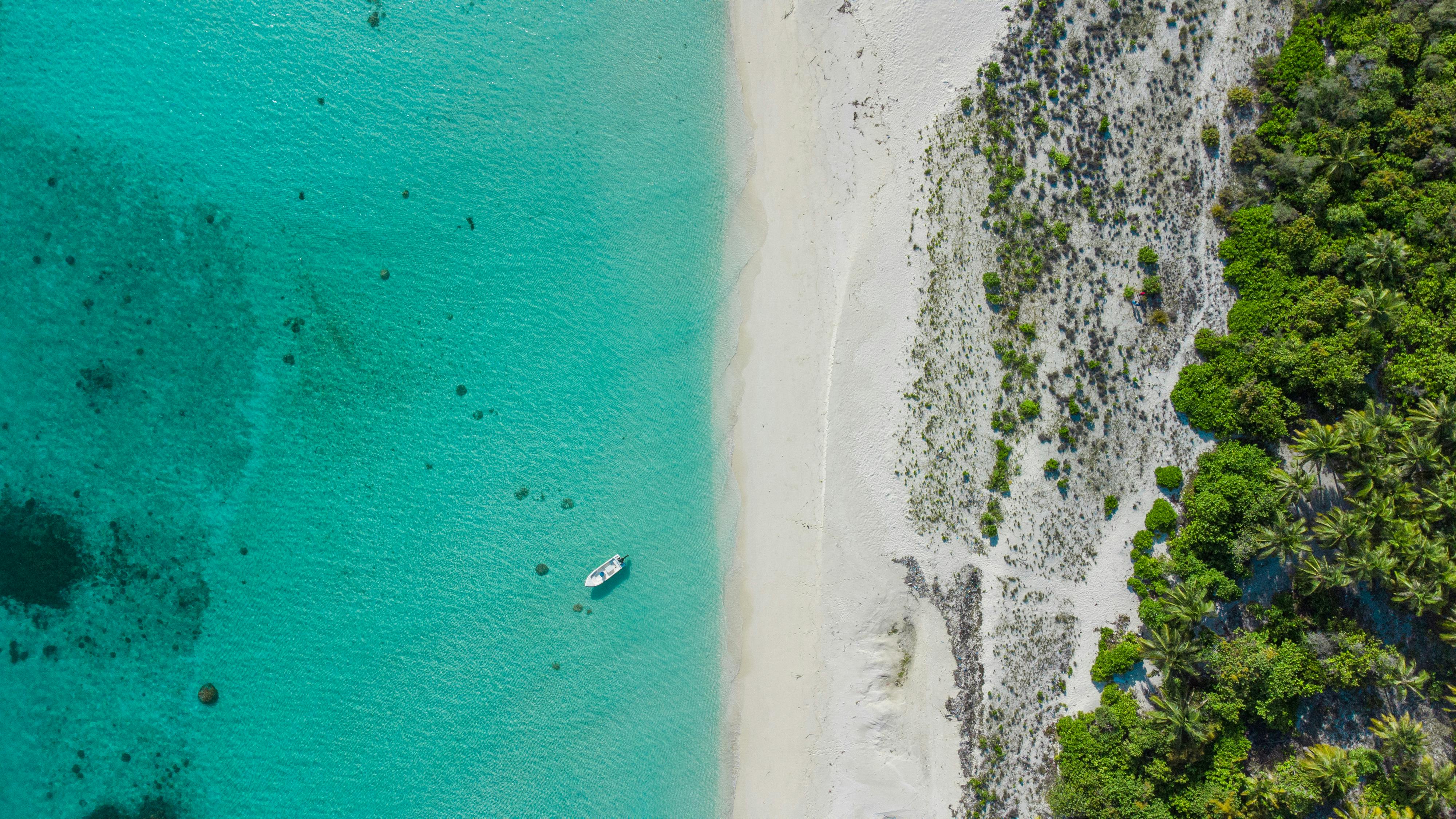 A stunning aerial shot of a boat on turquoise waters by a tropical beach.