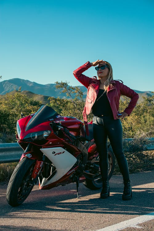 A woman in leather jacket posing next to a motorcycle