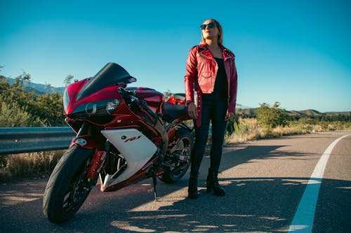 A woman in a leather jacket is standing next to a motorcycle