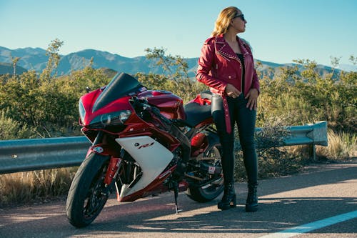 Woman in Red Jacket Standing with Motorbike on Road
