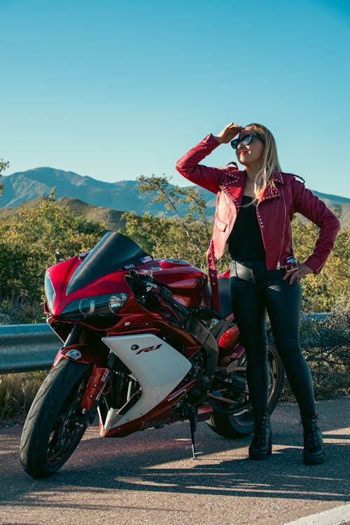 A woman in leather jacket posing next to a motorcycle