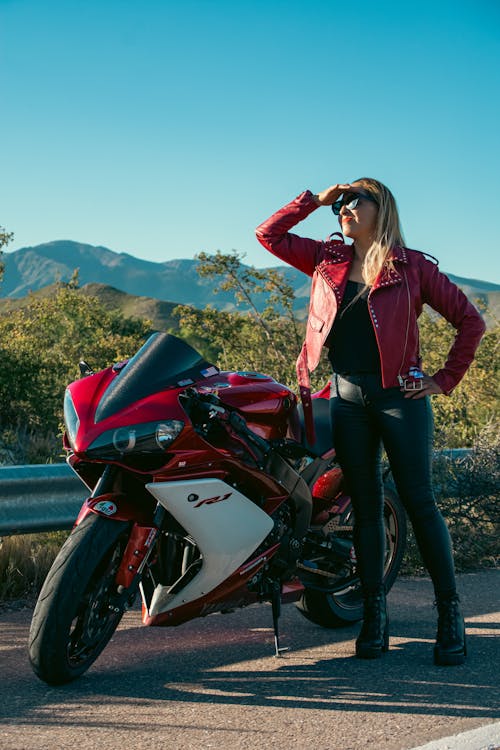 A woman in leather jacket posing next to a motorcycle