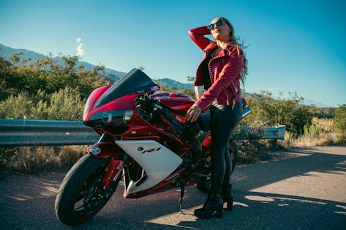 A woman in a red jacket is posing on a motorcycle