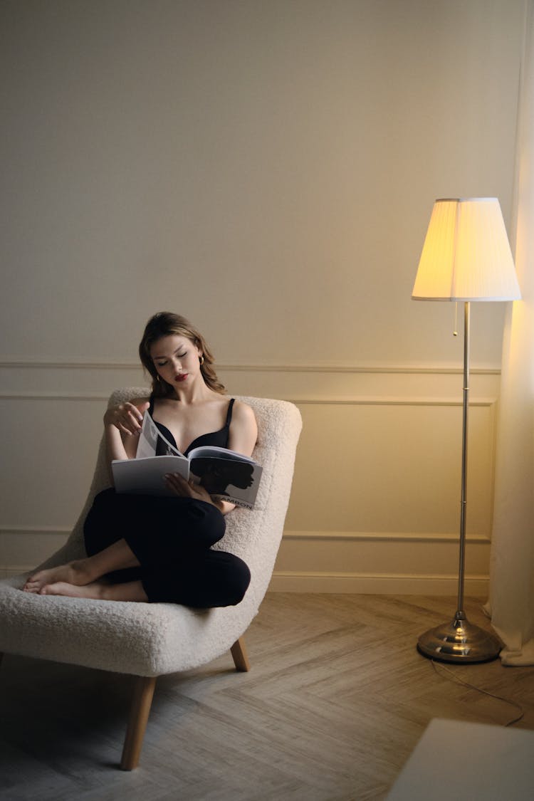 Woman Lying Down On Armchair And Reading Magazine