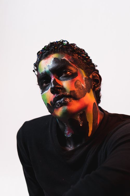 Free Artistic portrait of a man with a colorful painted face, captured in a studio setting. Stock Photo