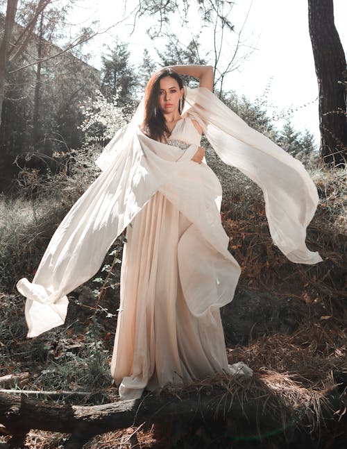 A woman in a long white dress is standing in the woods