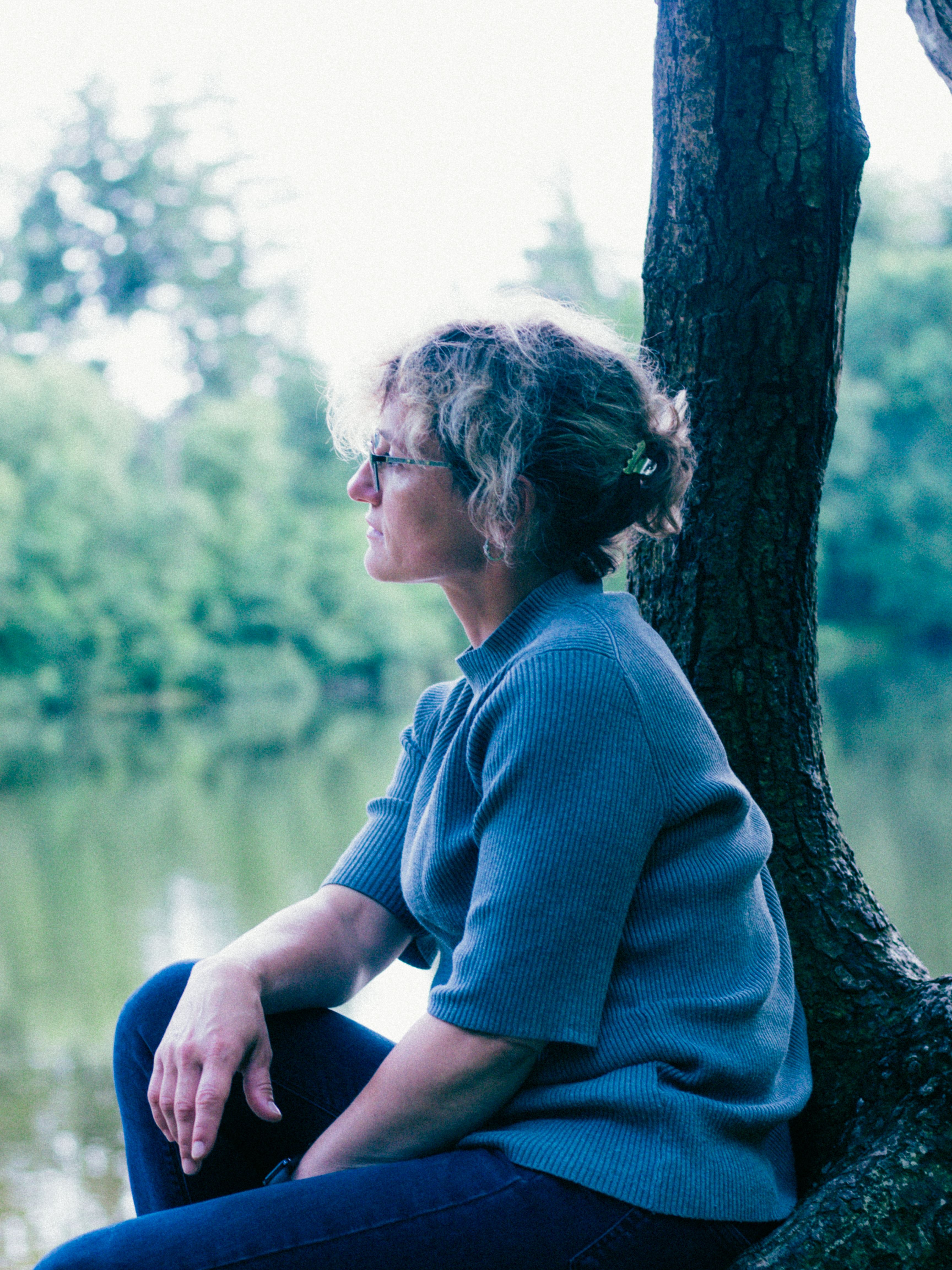 Side view of a woman sitting by a lake, embraced by nature's tranquility.