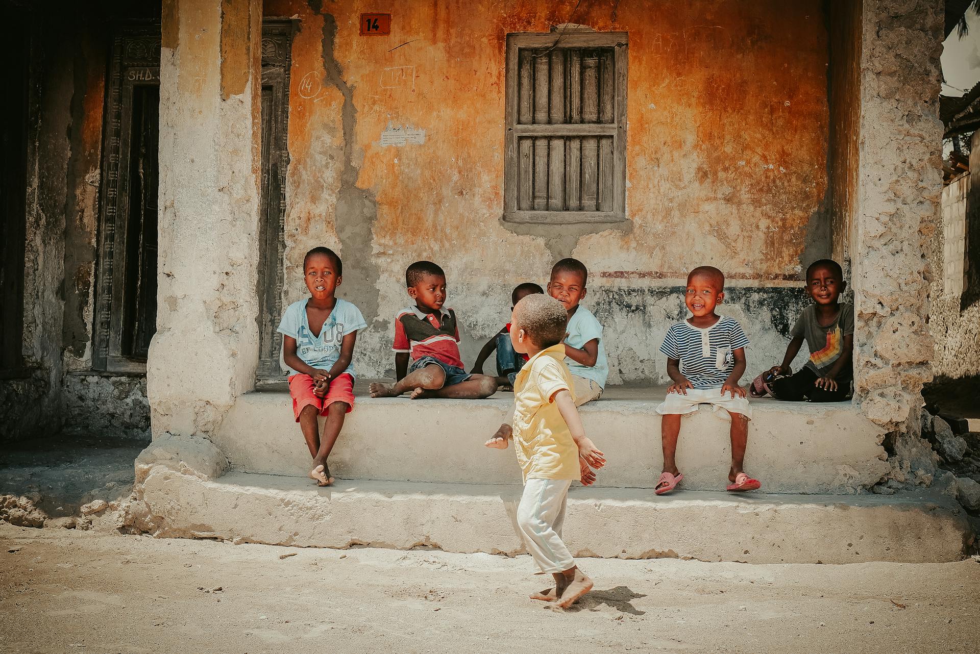 Group of smiling African children sitting and playing on weathered building steps.