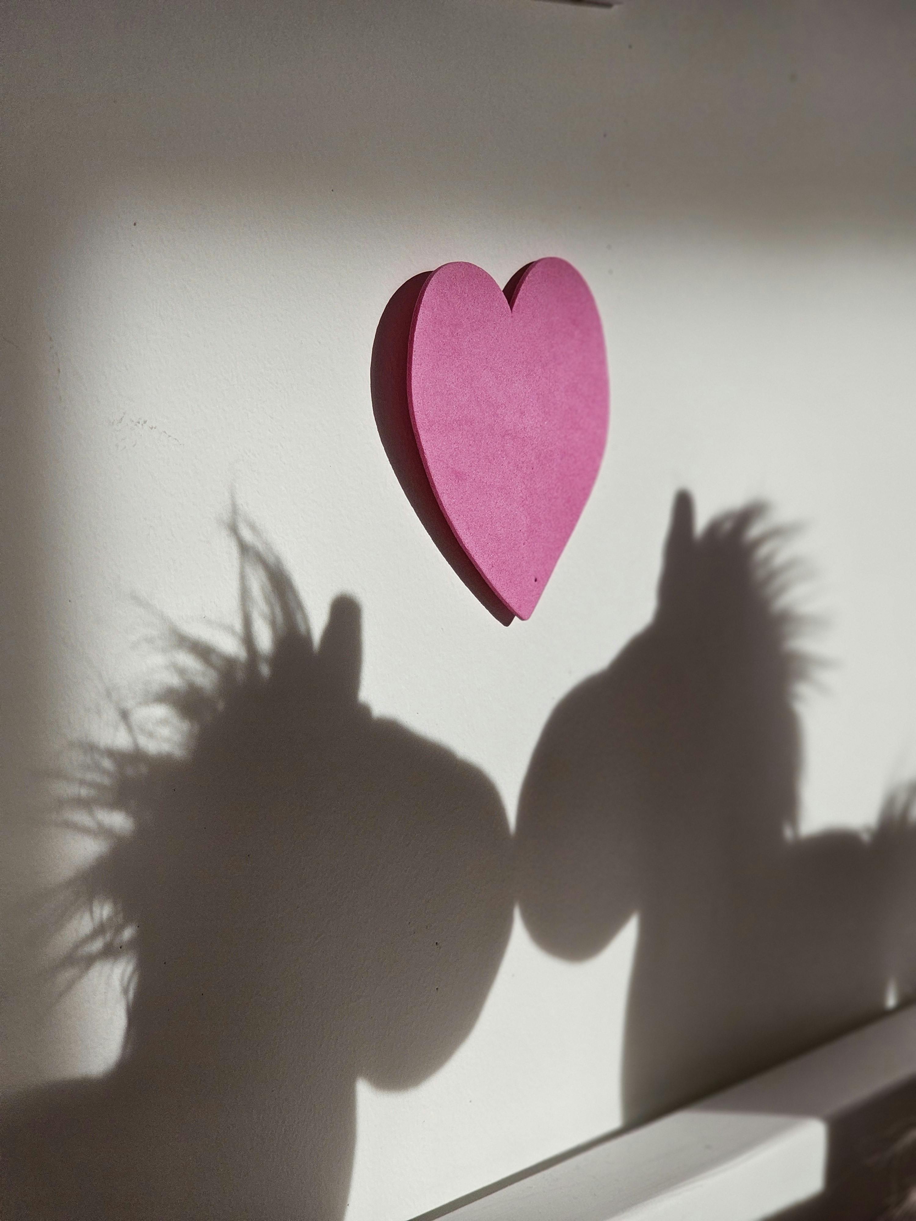 A pink heart with unicorn shadows cast on a white wall, creating a whimsical reflection.