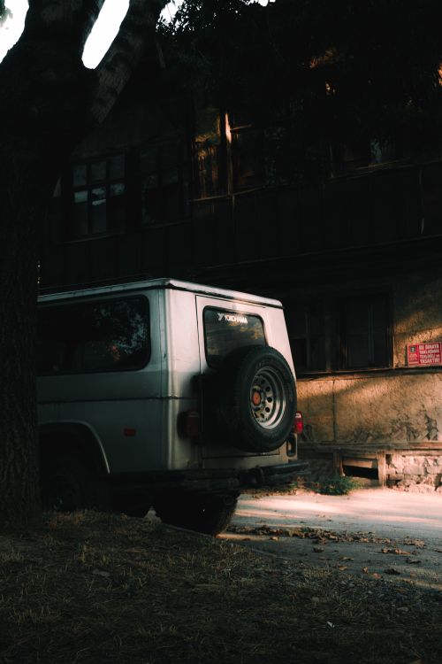 Free A vintage SUV is parked on a dimly lit urban street, creating a moody atmosphere. Stock Photo
