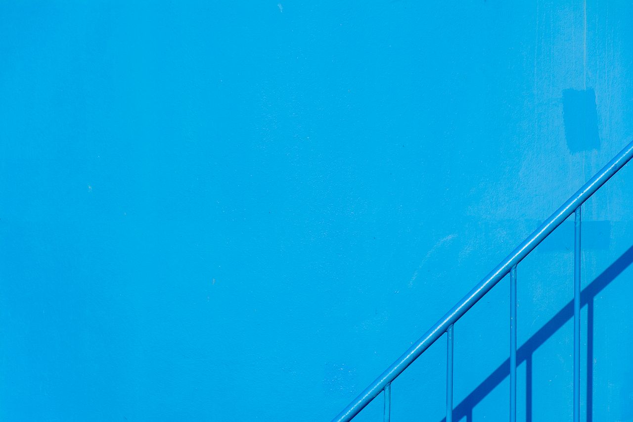 a minimalist photo of a blue wall with a shadowed stair handrail casti