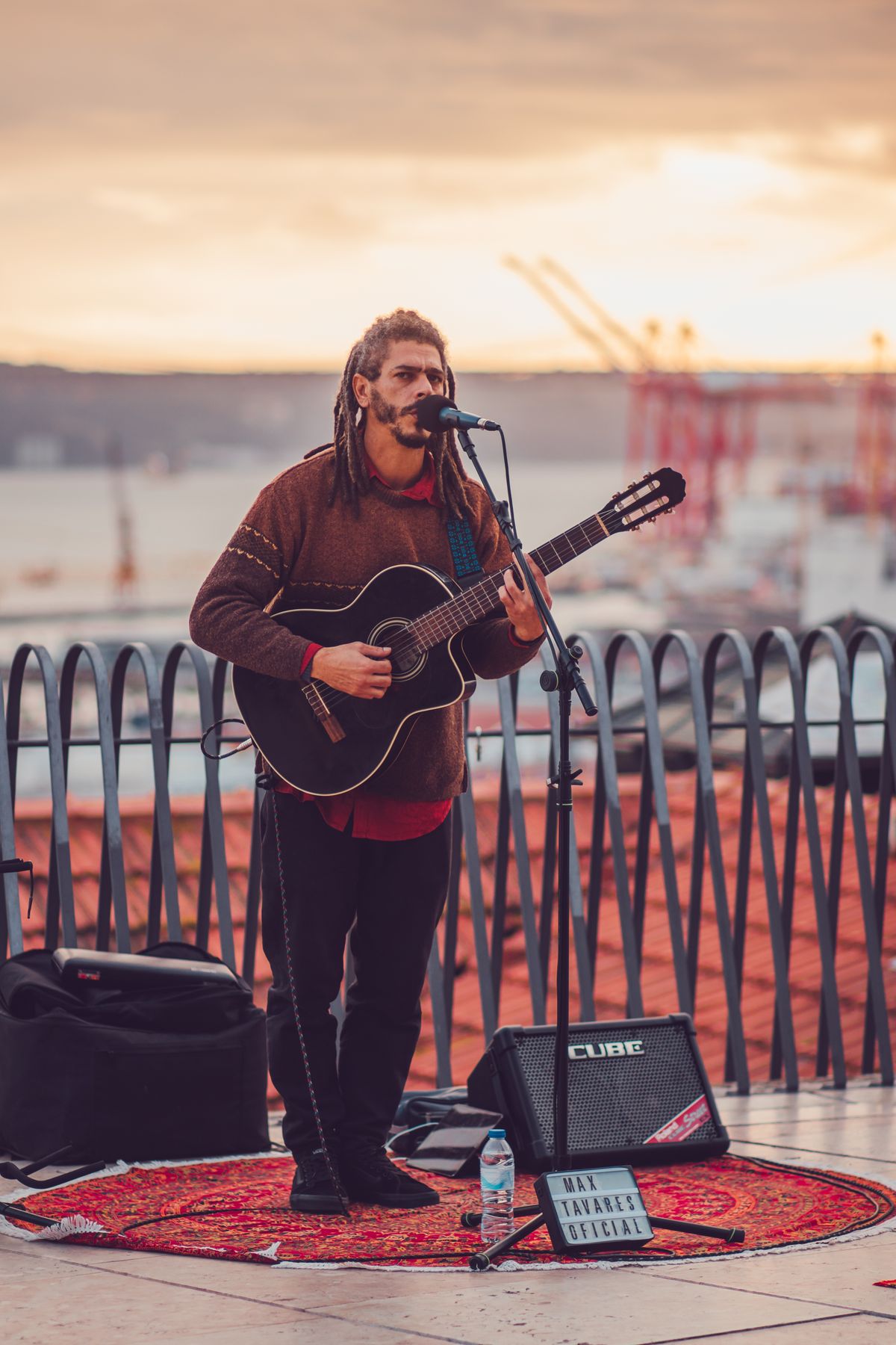 A street musician playing an acoustic guitar through a small amplifier at sunset