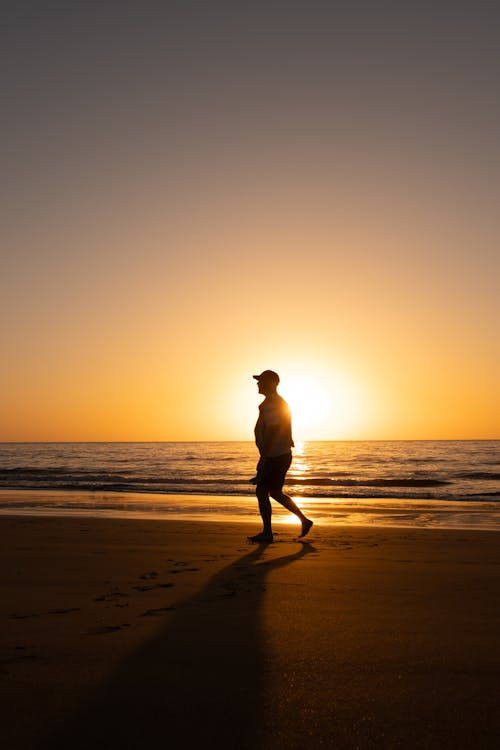 A silhouette of a person walking on the beach at sunset