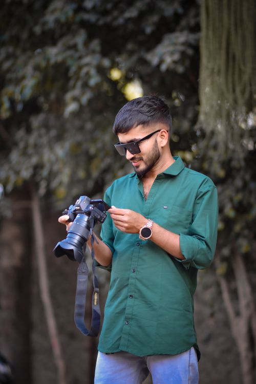 Free Young man in a green shirt with sunglasses, examining his Nikon camera outdoors on a sunny day. Stock Photo