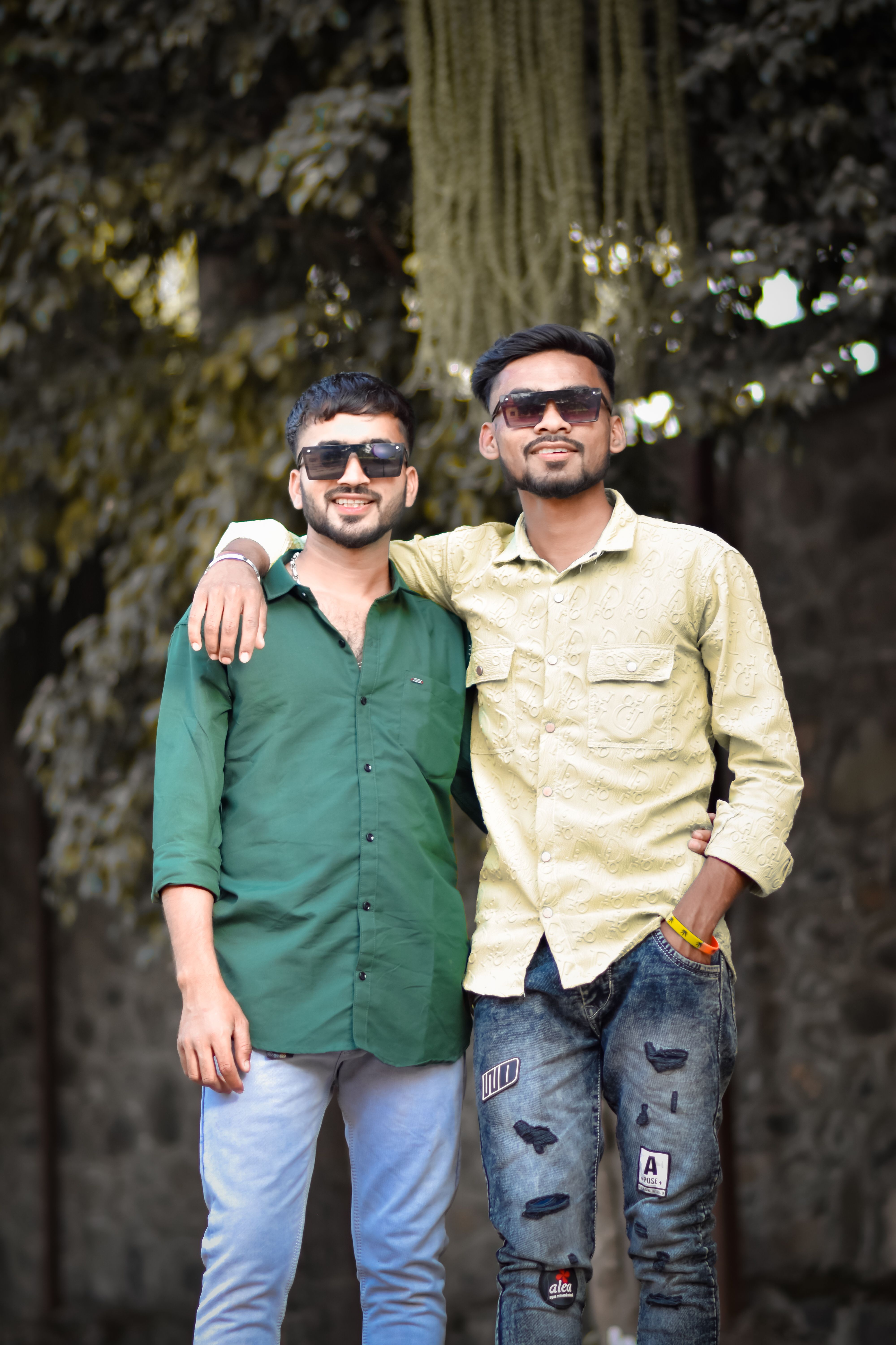 Two young men in casual attire smiling and posing confidently outdoors.
