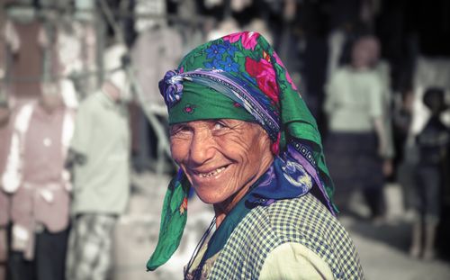Free Elderly woman with a colorful headscarf smiling outdoors, vibrant and cheerful. Stock Photo