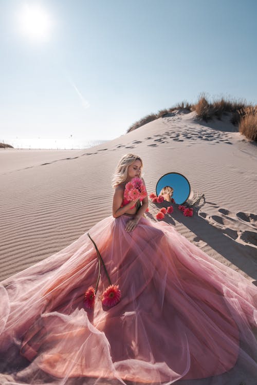 Woman in a Dress Sitting on a Sand Dune by a Mirror