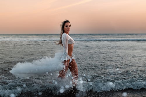 Woman in White Dress on Sea Shore at Sunset