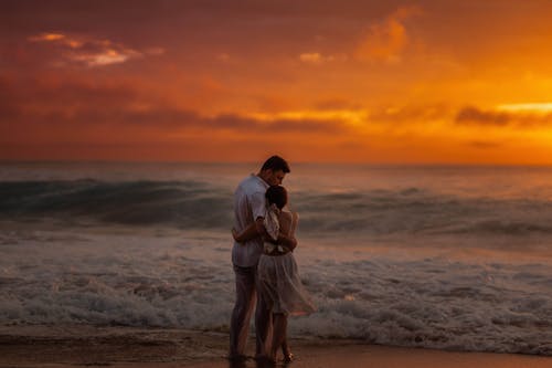 A couple standing on the beach at sunset