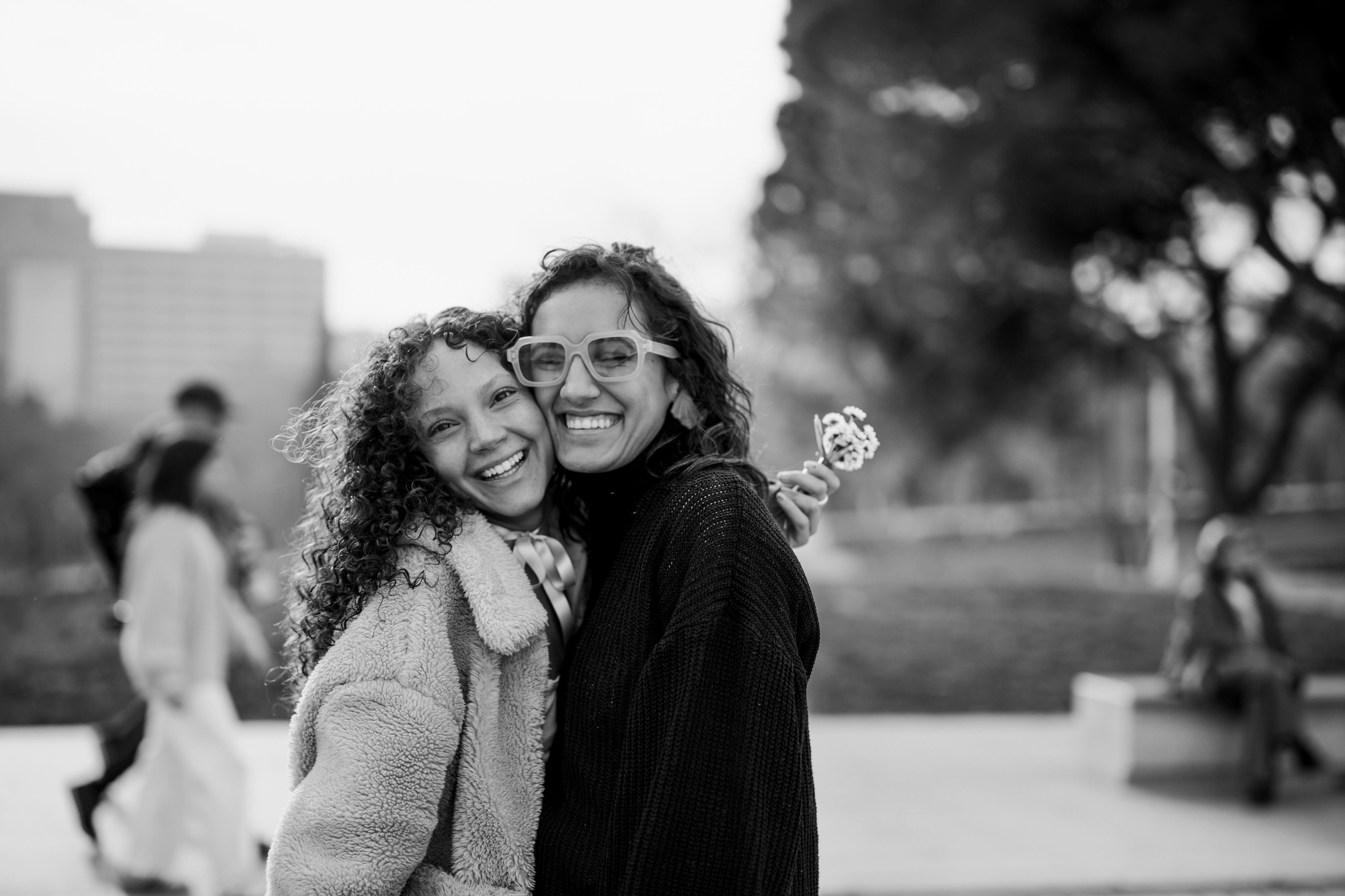 Two happy friends smiling outdoors, capturing a moment of joy in an urban setting.
