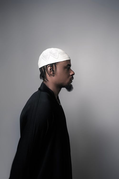 Free Profile portrait of a man in a black outfit and white cap, set against a neutral background. Stock Photo