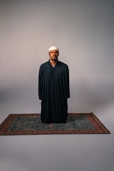 A man in traditional attire meditates on a prayer rug, in a serene minimalist setting.