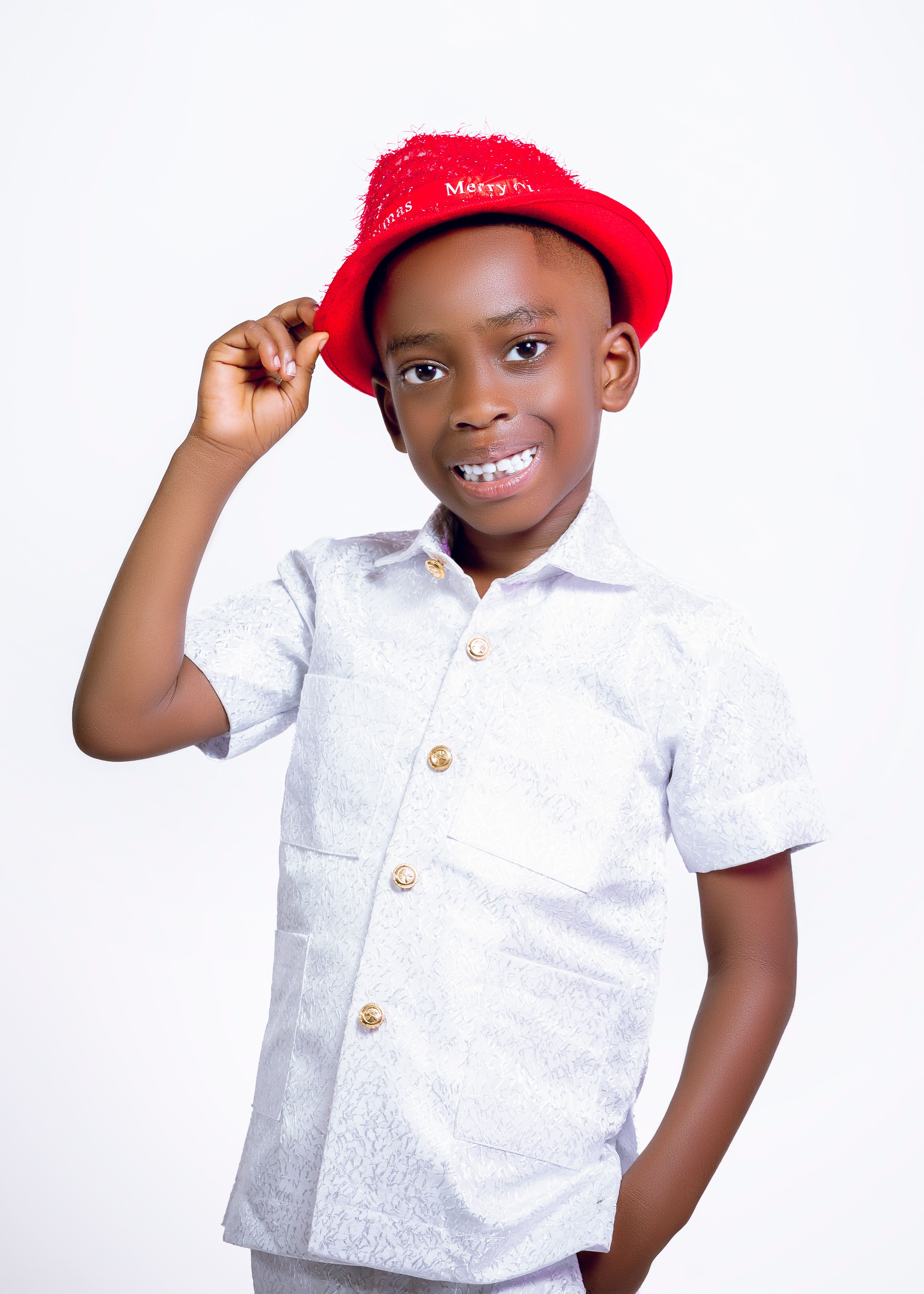 Smiling young boy wearing a red hat and white shirt, posing in a studio.