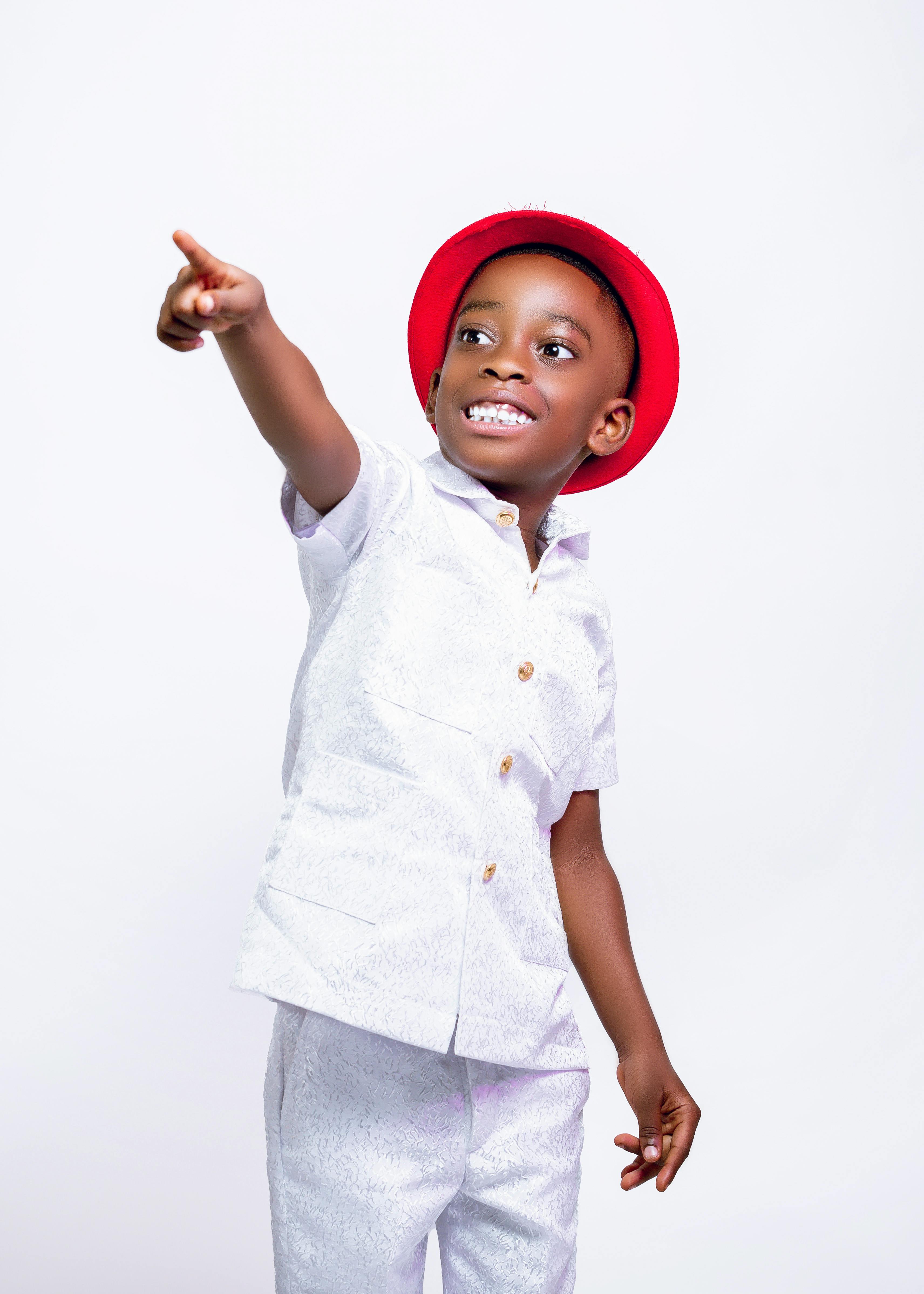 Happy child in red hat smiling and pointing at a blank space in a studio setting.